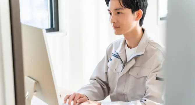 パソコンに向かって作業を行う作業着姿の男性