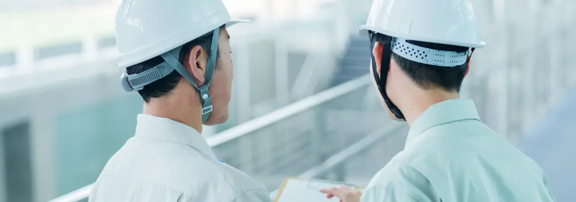 ヘルメットと作業着を着用して現場で打ち合わせを行う建築スタッフの後ろ姿