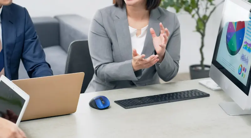 円グラフが表示されたモニターの前で手を動かしながら説明する女性スタッフ