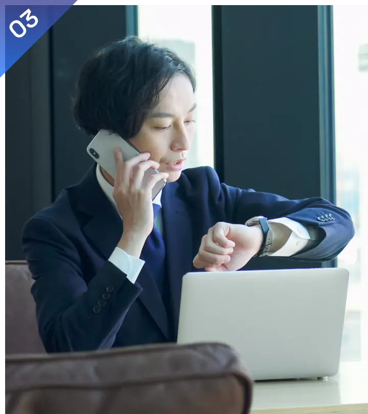 スマートフォンで通話しながら腕時計を確認するスーツ姿のビジネスパーソン