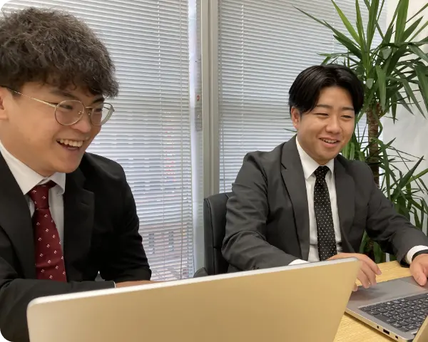 オフィスでパソコンを開き笑顔で打ち合わせをする男性社員たち